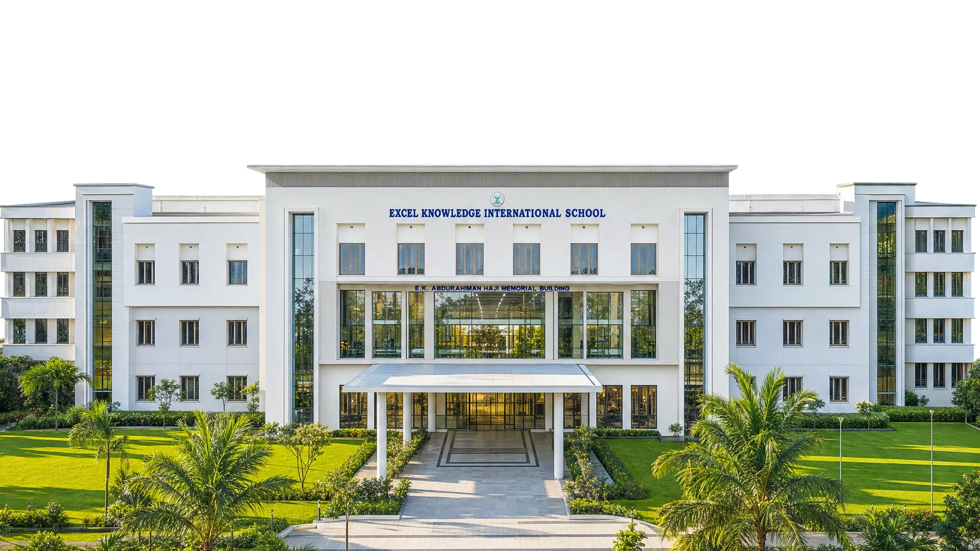 The full front facade of the EKIS school building, with lawns and palms along the approach